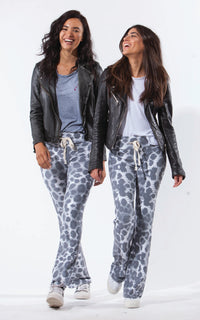 Two women wearing matching grey and white sweatpants with leather jackets on a white background